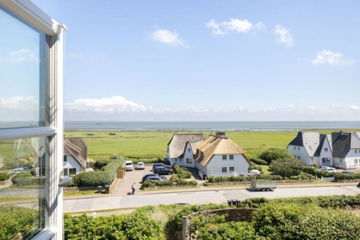 Reetdachhäuser auf Sylt mit Wattenmeer im Hintergrund
