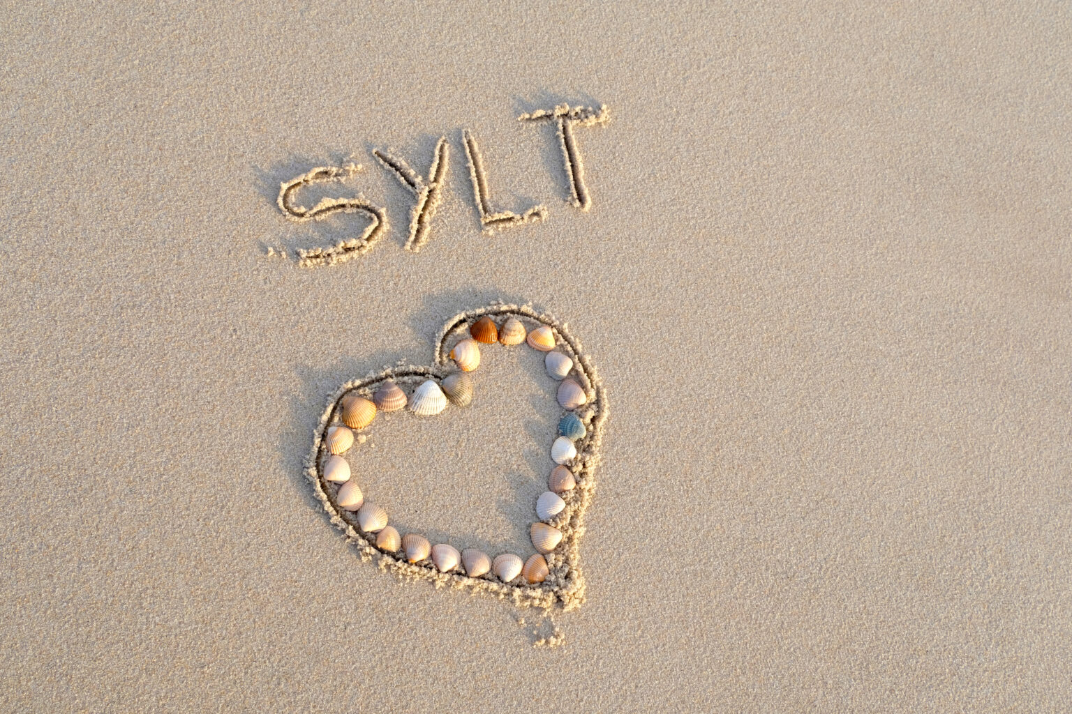 Herz aus Muscheln in den Strand gelegt. Schriftzug mit Sylt in den Sand geschrieben