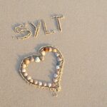 Herz aus Muscheln in den Strand gelegt. Schriftzug mit Sylt in den Sand geschrieben
