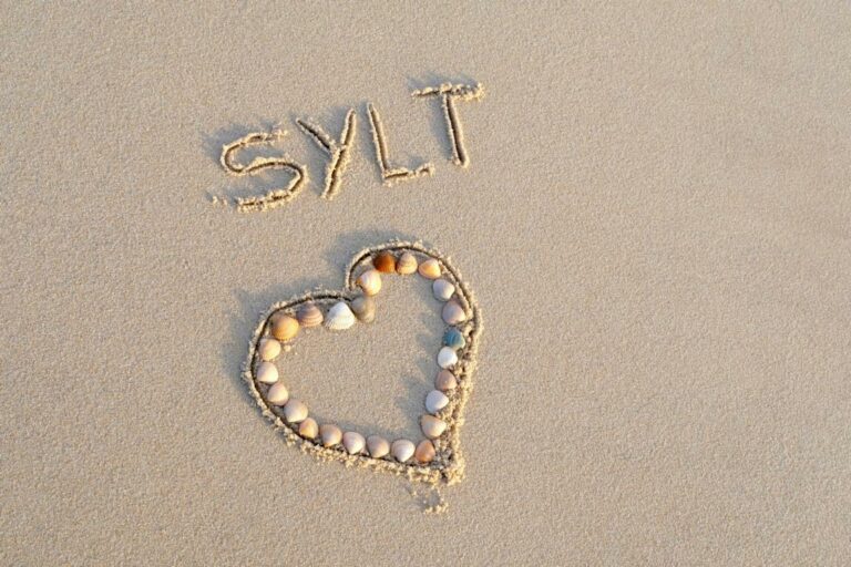 Herz aus Muscheln in den Strand gelegt. Schriftzug mit Sylt in den Sand geschrieben