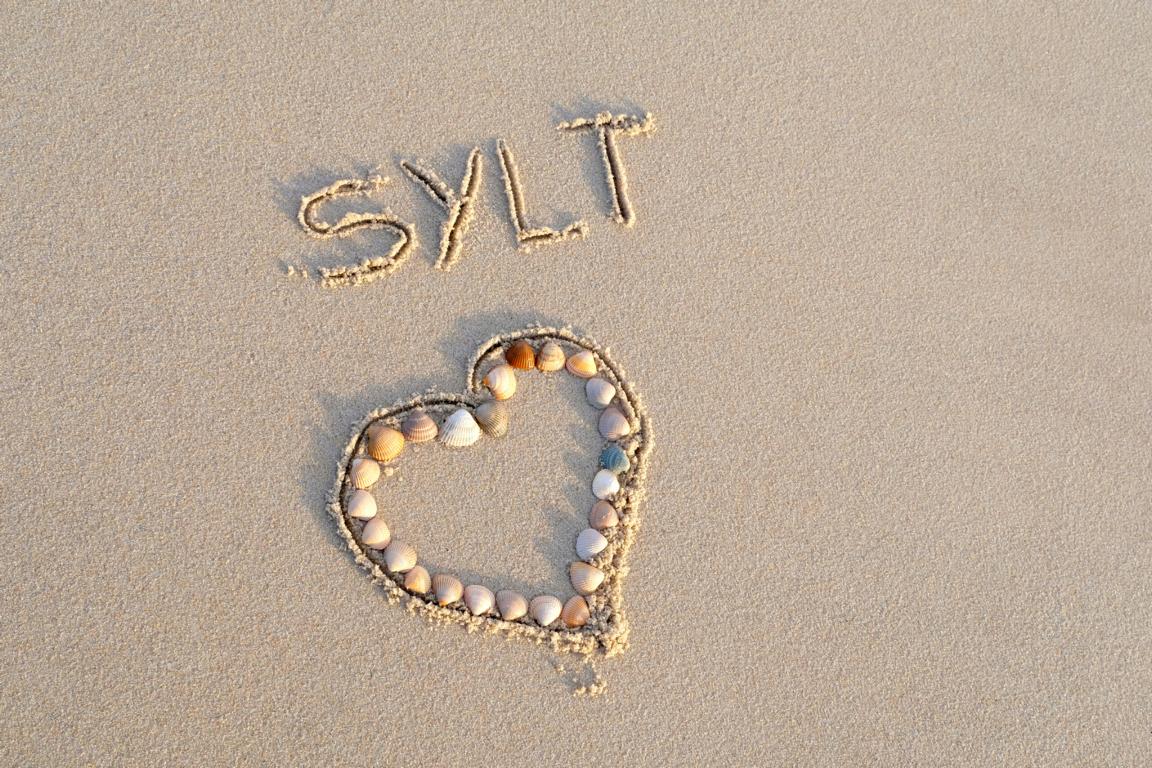 Herz aus Muscheln in den Strand gelegt. Schriftzug mit Sylt in den Sand geschrieben