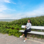 Gesichter von König Immobilien: Tammy Fürsch auf einer Bank vor Dünen und mit Blick auf das Meer