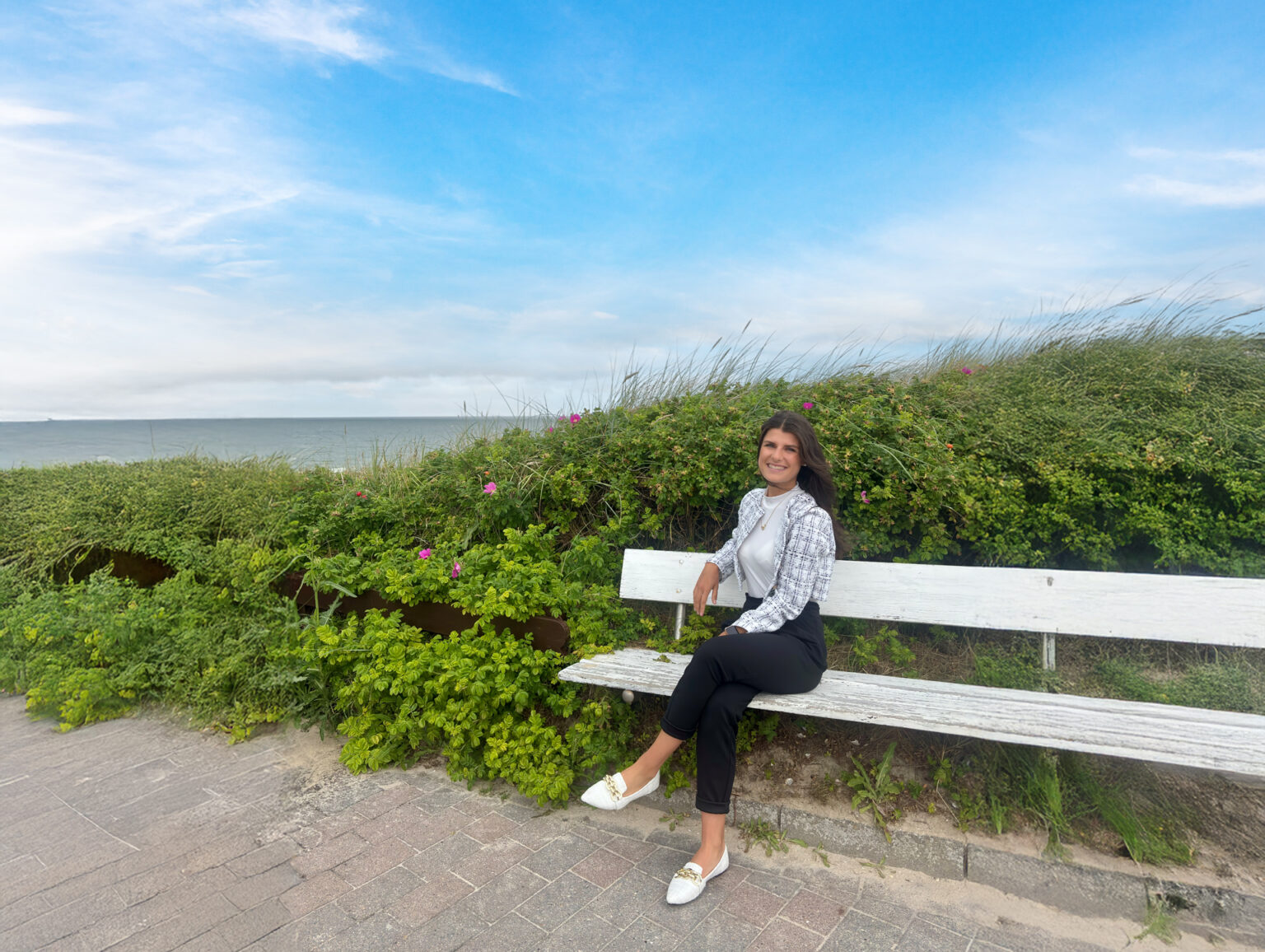 Gesichter von König Immobilien: Tammy Fürsch auf einer Bank vor Dünen und mit Blick auf das Meer