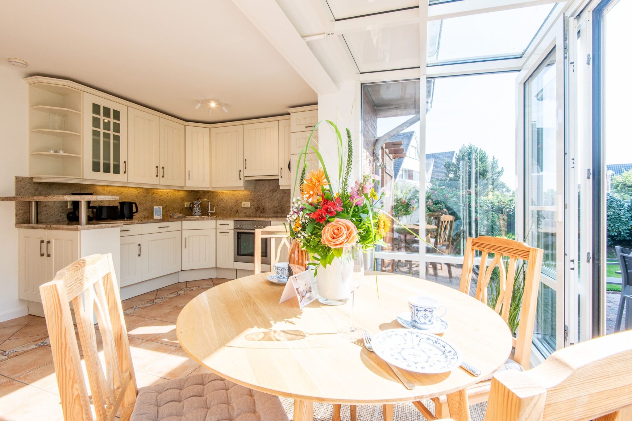 gedeckter Tisch im Wintergarten und Küche im Hintergrund in einem Ferienhaus auf Sylt